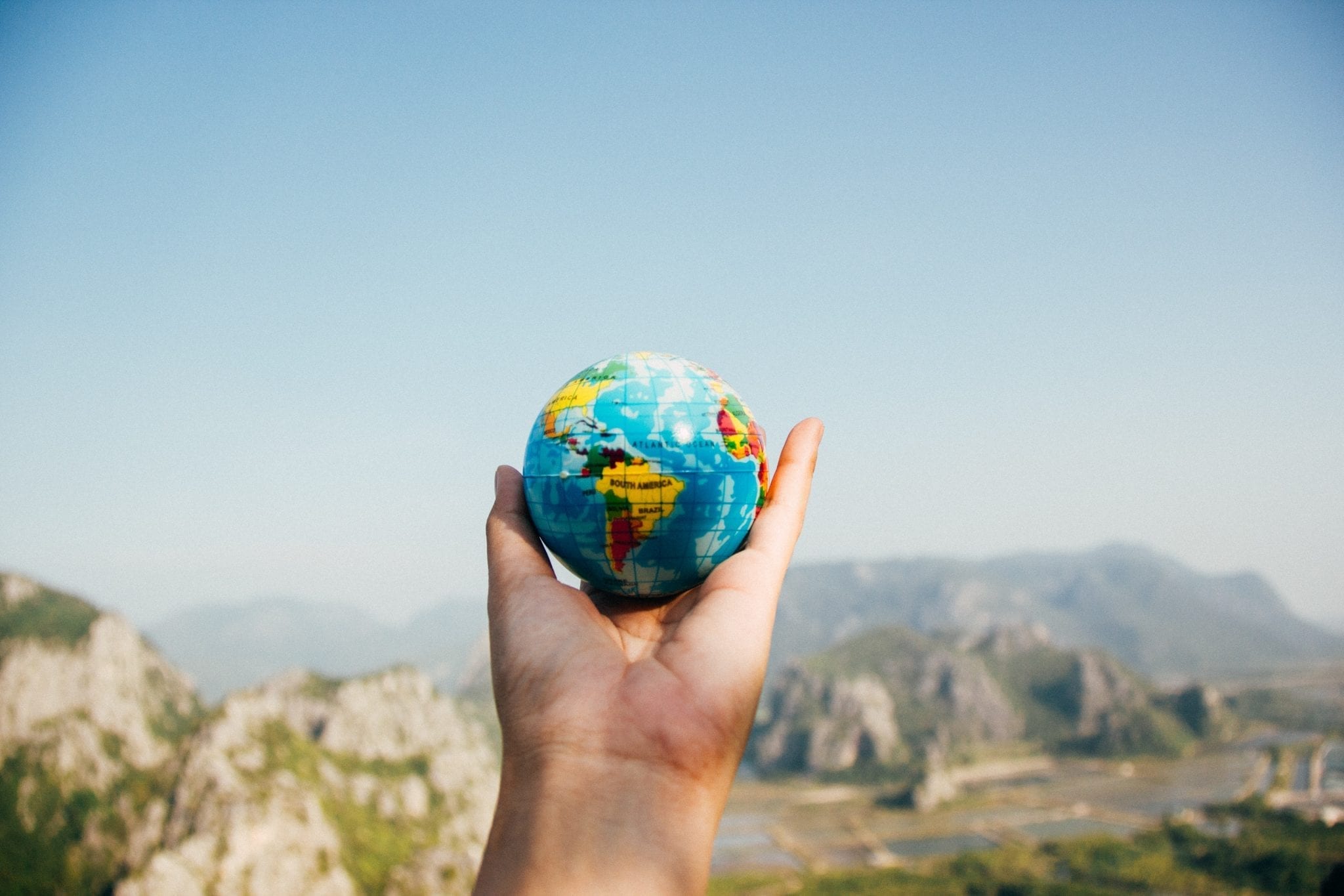 Outstretched hand holding a globe looking with mountains in the back